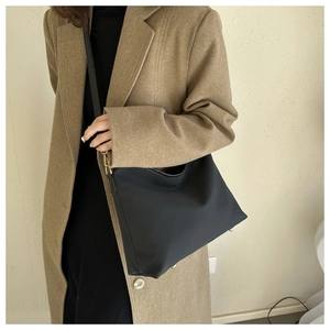 Close-up of minimalist black tote bag with gold hardware on camel wool coat
