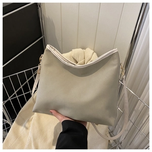 Detail of light olive leather tote with white trim and adjustable strap on a metal rack