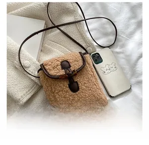 Mini sac bandoulière marron en sherpa avec bordure cuir et bouton corne près d'un mobile