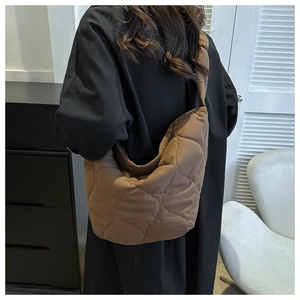 Close-up of brown quilted crescent shoulder bag with puffy texture and wide strap