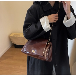 Detail of dark brown glossy leather crossbody bag with gold chain strap and metal lock