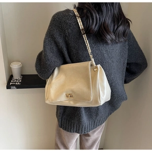 Detail of minimalist cream leather crossbody bag with gold chain strap and rotary lock