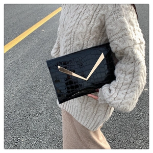 Detail of a black crocodile-pattern envelope clutch bag with V-shaped gold metal trim