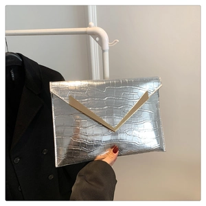 Detail of silver crocodile-embossed envelope clutch with gold V-shaped metal trim