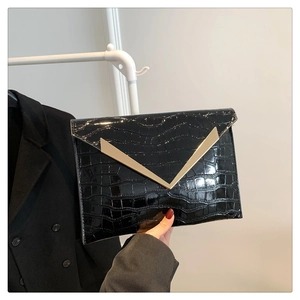 Close-up of black crocodile pattern clutch bag with elegant golden V-shaped buckle