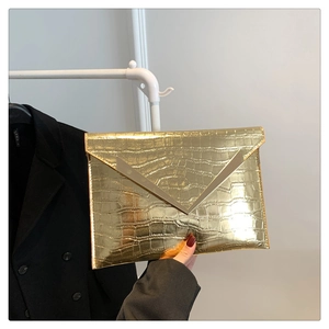 Close-up of gold envelope clutch bag with crocodile texture and V-shaped metal trim