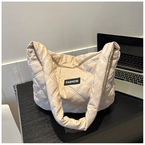 Détail du sac fourre-tout beige matelassé avec étiquette de mode sur un bureau épuré