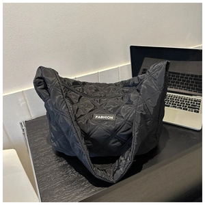 Détail du sac fourre-tout noir matelassé en nylon posé sur une surface en bois sombre
