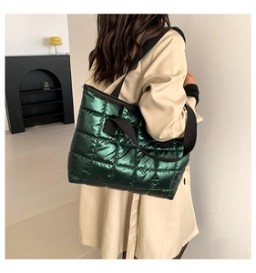 Detail of metallic green quilted tote bag featuring wide black shoulder straps on model