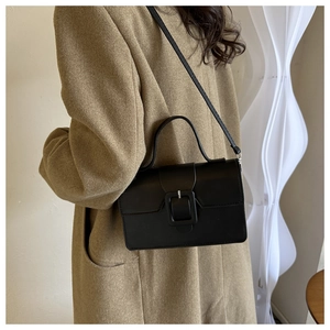 Sac à main en cuir noir avec poignée et bandoulière, porté sur un manteau en laine