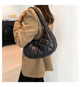 Close-up of black quilted puffer crescent bag worn over the shoulder with gold zipper