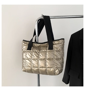 Detail of gold quilted tote bag with metallic finish and black webbing handles on a rack