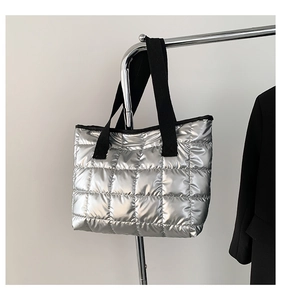 Detail of silver quilted tote bag featuring metallic finish and wide black straps