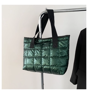 Detail of dark green quilted tote bag with glossy metallic finish and black wide handles