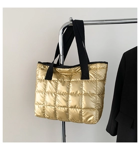Detail of metallic gold quilted tote bag with black woven handles on a hanger