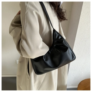 Detail of black pleated cloud shoulder bag with matte leather texture on beige background
