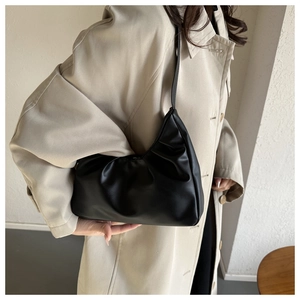 Macro detail of black ruched leather shoulder bag texture on beige trench coat