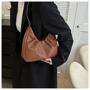 Detail einer braunen Hobo-Tasche mit Wolkenfalten, getragen von einem Model im schwarzen Anzug