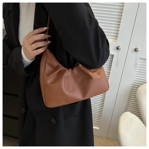 Detailansicht der karamellbraunen Cloud-Tasche mit Falten an einem Model im Anzug