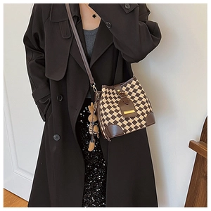 Detail of woven checkerboard bucket bag with brown leather trim and cute bear charm
