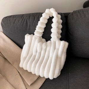 White faux fur tote bag with vertical stripes and plush ball handles on sofa