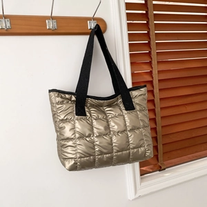 Stylish metallic gold quilted tote bag with black strap hanging on a wooden hook