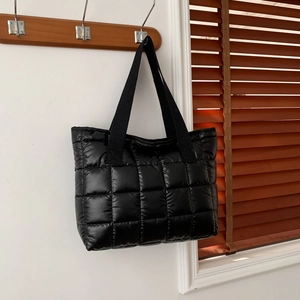 Fashionable black quilted puffer tote bag with long straps hanging on a wooden hook