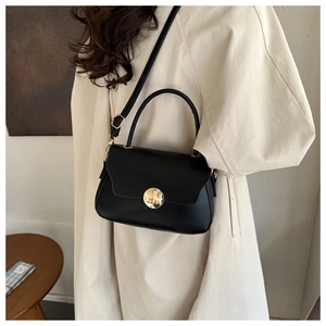 Detail of black crossbody bag on model showing adjustable strap and golden round buckle