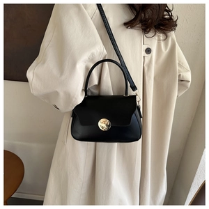 Detail of minimalist black crossbody bag with wavy flap and golden clasp on beige coat