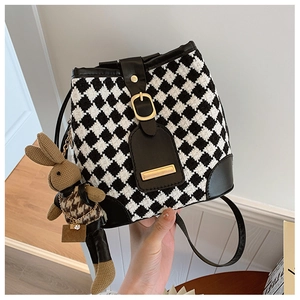 Close-up of retro houndstooth bucket bag with leather trim and cute rabbit doll charm