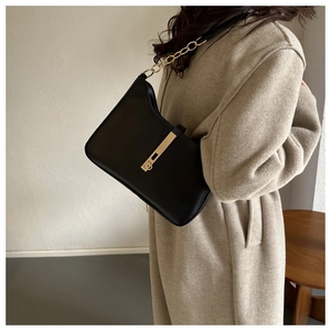 Detailed view of the black leather underarm bag with gold chain strap worn on an oat coat