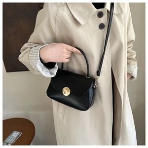 Close-up of minimalist black handbag with polished gold buckle on a beige trench coat