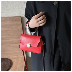 Detail of red crossbody bag with gold round clasp against a black trench coat