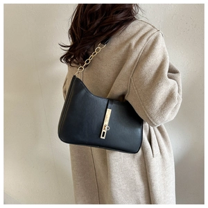 Close-up of minimalist black half-moon shoulder bag with golden chain and metal buckle