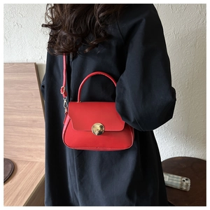 Detail of red minimalist crossbody bag featuring golden round buckle and adjustable strap