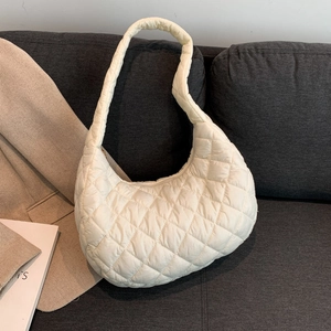 Quilted white shoulder bag with classic diamond stitch pattern on a gray sofa