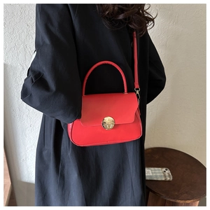 Detail of red leather crossbody bag featuring a round gold buckle and black coat contrast