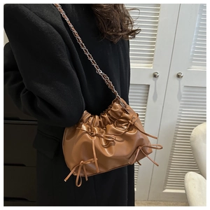 Détail d'un sac cabas marron plissé avec nœuds et bandoulière chaîne porté par un mannequin