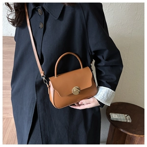 Brown leather crossbody bag with round gold buckle shown on a black trench coat