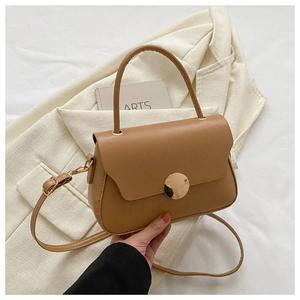 Detail of tan faux leather handbag with gold circular buckle on beige blazer
