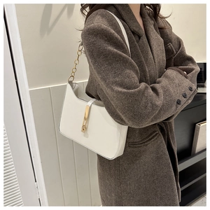 Close-up of white leather underarm bag with gold metal buckle and chain on brown coat