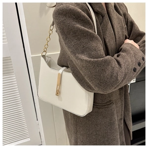 White minimalist underarm bag with gold metal buckle and chain strap on a brown coat