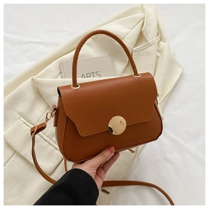 Detail of caramel faux leather handbag featuring a round gold magnetic clasp on a blazer