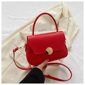 Detail of red leather crossbody bag featuring large circular gold metal buckle and handle