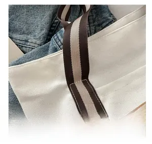 Dettaglio della borsa tote in tela con manici a righe e toppa in pelle con cuciture