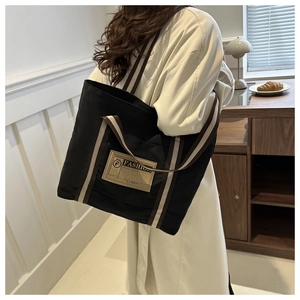 Dettaglio della borsa tote in tela nera con tracolla a righe indossata a spalla