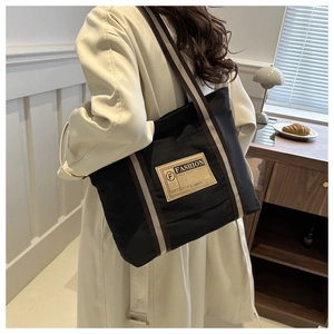 Dettaglio della borsa tote in tela nera con etichetta moda e tracolla a righe sulla modella