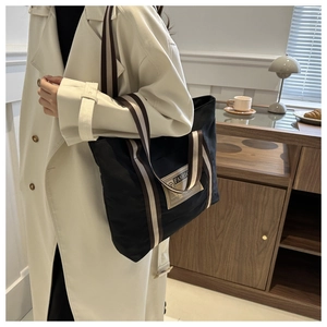 Dettaglio della borsa tote in tela nera con manici a righe in una scena lifestyle