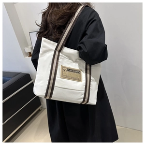 Dettaglio della borsa tote in tela bianca con manici a righe e toppa moda sulla spalla