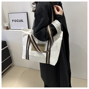 Dettaglio della borsa tote in tela con manici a righe e patch vintage fashion sul modello